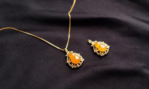 Jade jewelry setting featuring orange-yellow jade teardrop pendant in gold floral setting